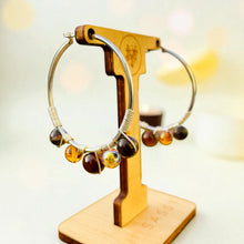 Load image into Gallery viewer, Pair of hoop earrings with beads on a wooden stand against a blurred background