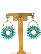 Load image into Gallery viewer, Turquoise sunflower earrings on a wooden display stand with a logo.