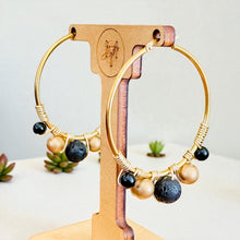 Load image into Gallery viewer, Gold hoop earrings with black and gold beads on a wooden stand.