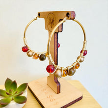 Load image into Gallery viewer, Gold hoop earrings with colorful beads on a wooden stand with 'SASSY' branding.