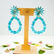 Load image into Gallery viewer, Turquoise beaded earrings on a wooden display stand with &#39;MISSASSY&#39; branding, surrounded by flowers.
