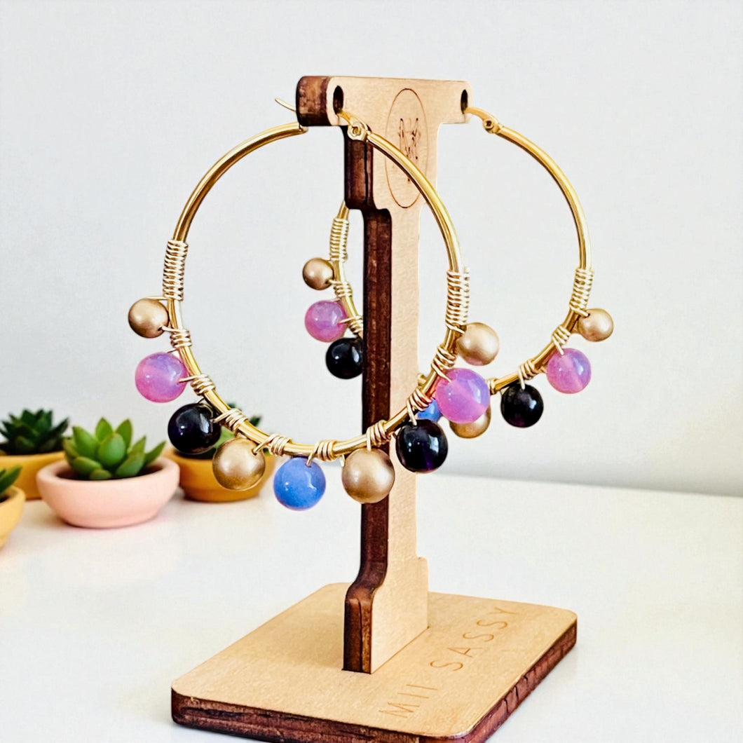 Gold hoop earrings with colorful beads on a wooden stand against a light background