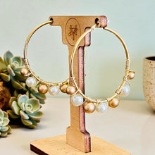 Load image into Gallery viewer, Gold hoop earrings with pearls on a wooden stand against a light background
