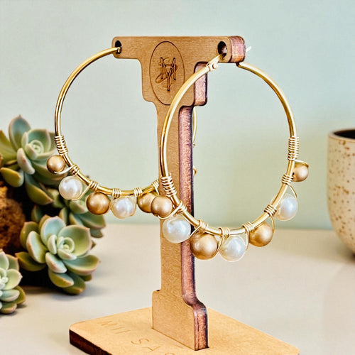 Gold hoop earrings with pearls on a wooden stand against a light background