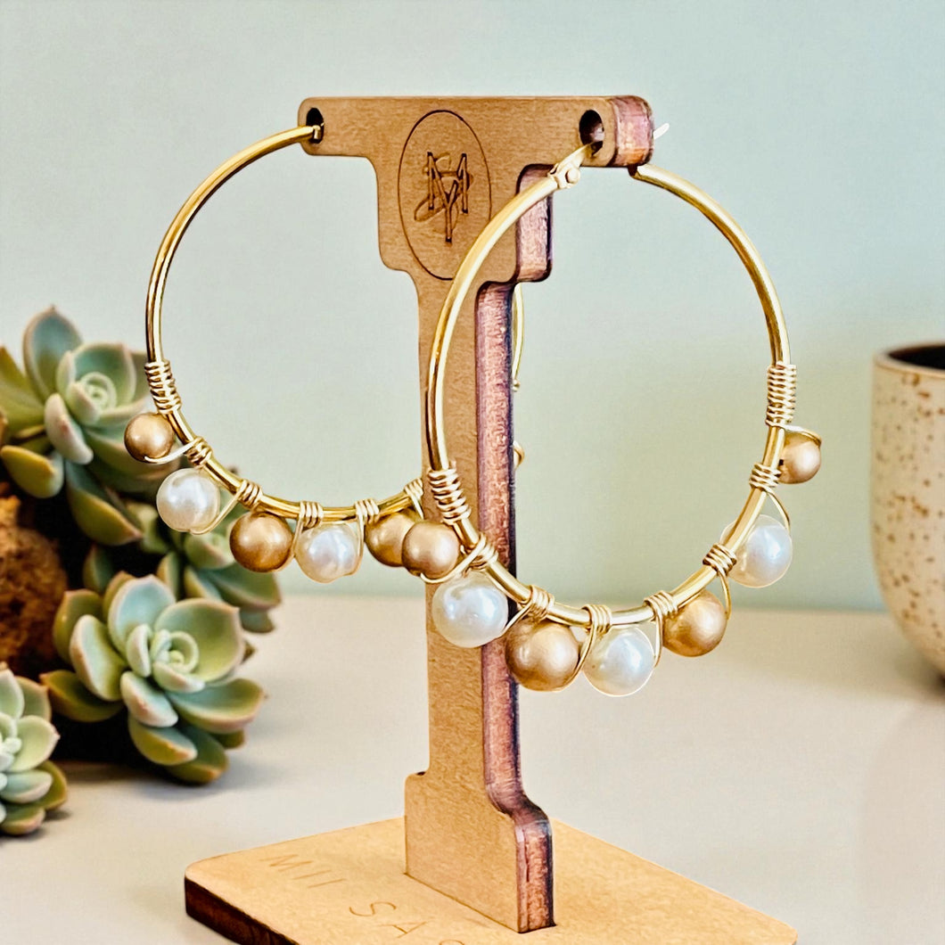 Gold hoop earrings with pearls on a wooden stand against a light background