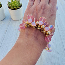 Load image into Gallery viewer, Hand wearing a bracelet with pink and gold beads on a light wooden surface.
