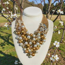 Load image into Gallery viewer, Gold and pearl necklace on a mannequin with a natural background of trees and flowers
