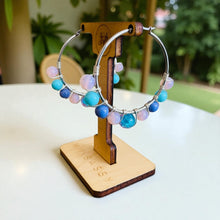 Load image into Gallery viewer, Colorful beaded hoop earrings on a wooden stand with a blurred green background
