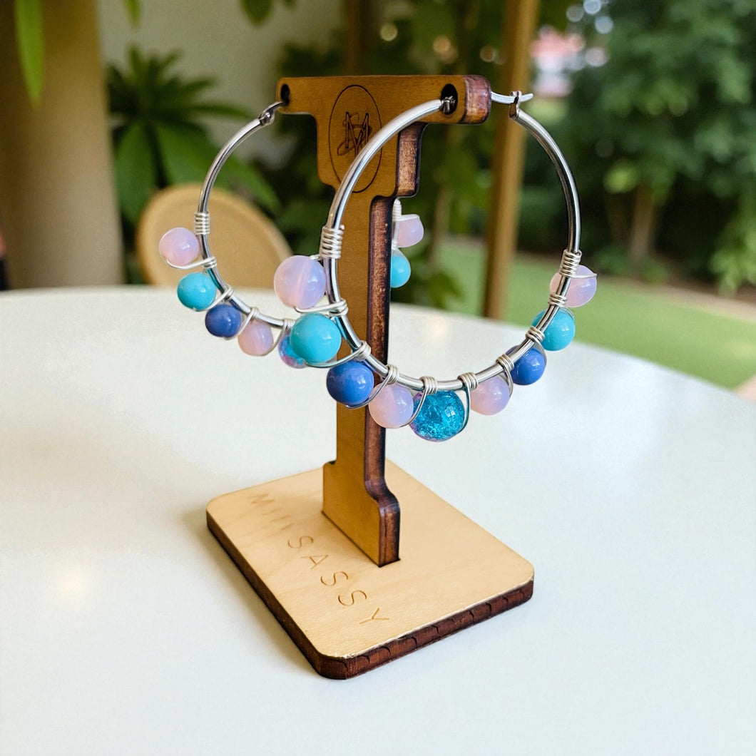 Colorful beaded hoop earrings on a wooden stand with a blurred green background