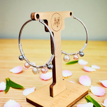Load image into Gallery viewer, Silver hoop earrings with beads on a wooden stand with pink petals and green leaves on a wooden surface.
