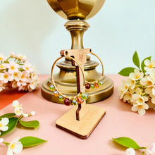 Load image into Gallery viewer, Gold earring stand with a gold earring on a pink surface with flowers
