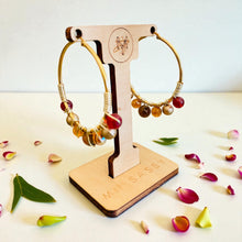 Load image into Gallery viewer, Gold hoop earrings with beads on a wooden stand with &#39;MIL SASS&#39; branding, surrounded by flower petals.
