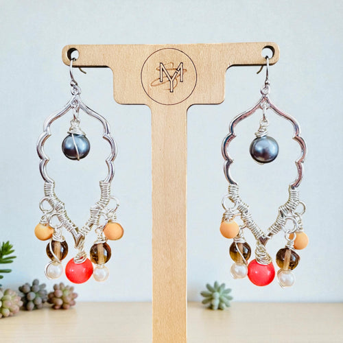 Pair of earrings with colorful beads on a wooden stand with a brand logo. Pair of silver earrings with colorful beads on a wooden stand with blurred natural background
