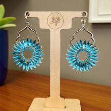 Load image into Gallery viewer, Blue floral earrings on a wooden display stand with a blurred background. Turquoise sunflower earrings on a wooden display stand with a blurred outdoor background.
