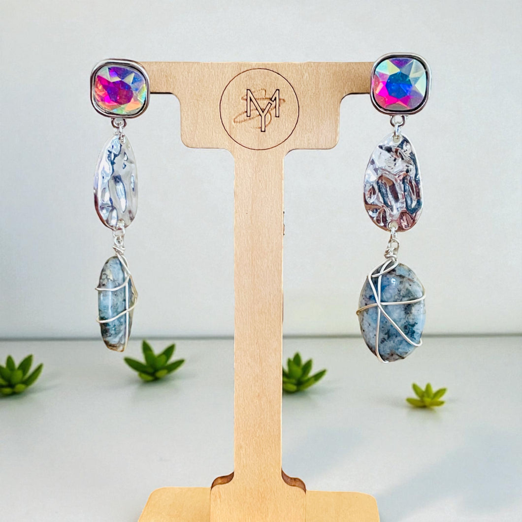 Pair of earrings with colorful stones on a wooden stand with a brand 
logo. 
wire wrapped earrings, handmade earrings, beaded drop earrings, multicolor jewelry, artisan earrings, boho chic earrings, unique handmade gifts, statement earrings, silver dangle earrings, colorful jewelry for women